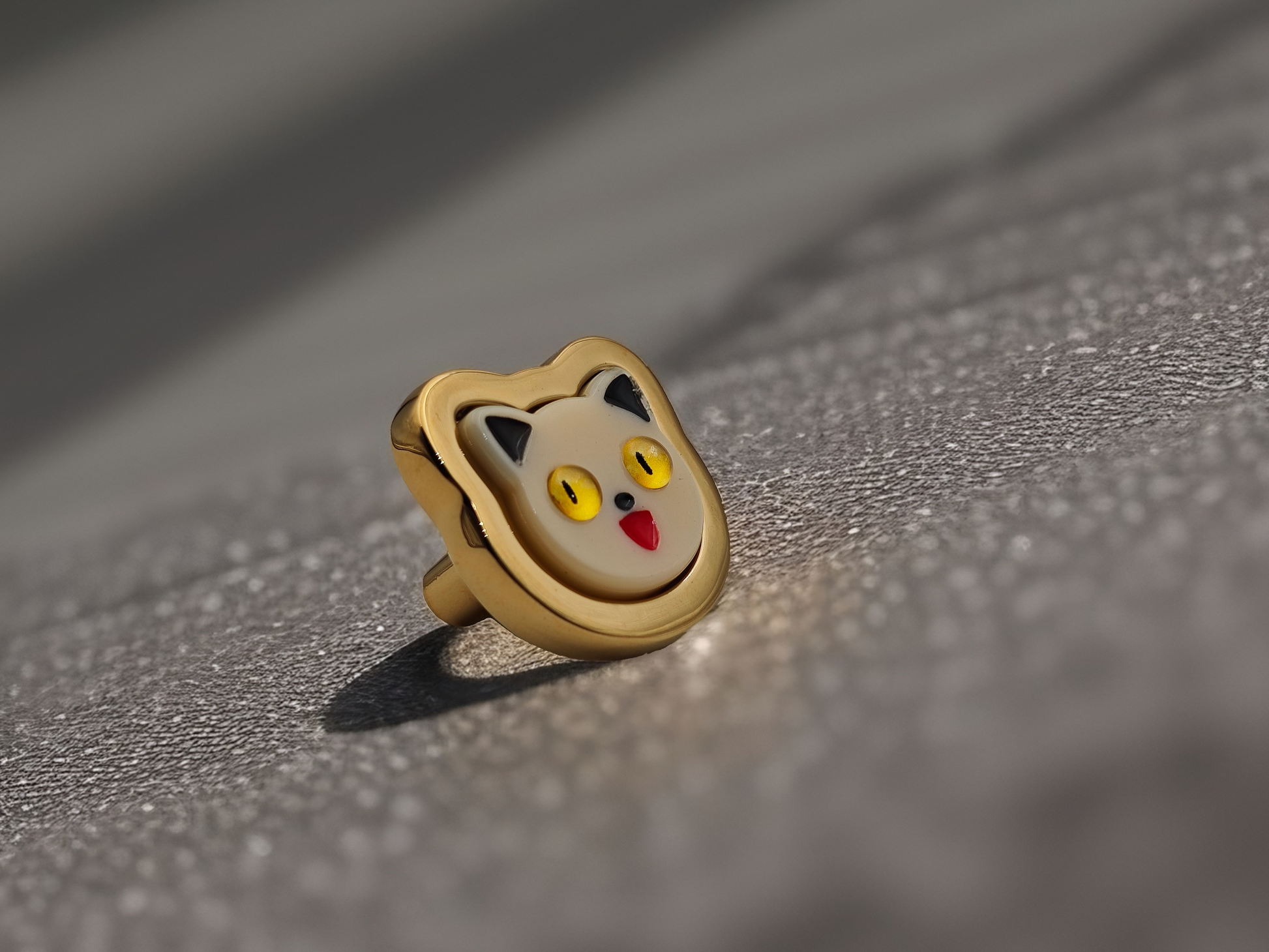 A gold-colored metal cabinet handle designed to look like a cat's face, placed on a reflective surface.