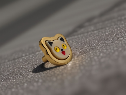 A gold-colored metal cabinet handle designed to look like a cat's face, placed on a reflective surface.