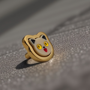 A gold-colored metal cabinet handle designed to look like a cat's face, placed on a reflective surface.